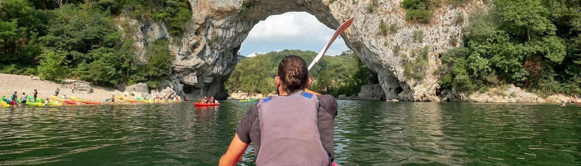 On the tour "Maxi-Discovery 13km" in Ardèche, a couple is passing under the famous Pont d'Arc arch whilst sitting in a high-quality canoe rented at Aigue Vive.