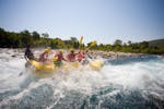 Eine Gruppe von Freunden sitzen im Raft und raften den Fluss hinab beim Rafting auf der Iller für Junggesellenabschiede (ab 10 Personen) mit MB Events & Adventures Allgäu & Bodensee.