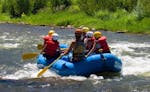 Eine Gruppe von Freunden sitzt im Raft und fährt den Fluss hinab beim Rafting auf der Iller für Jugendgruppen mit MB Events & Adventures Allgäu & Bodensee.