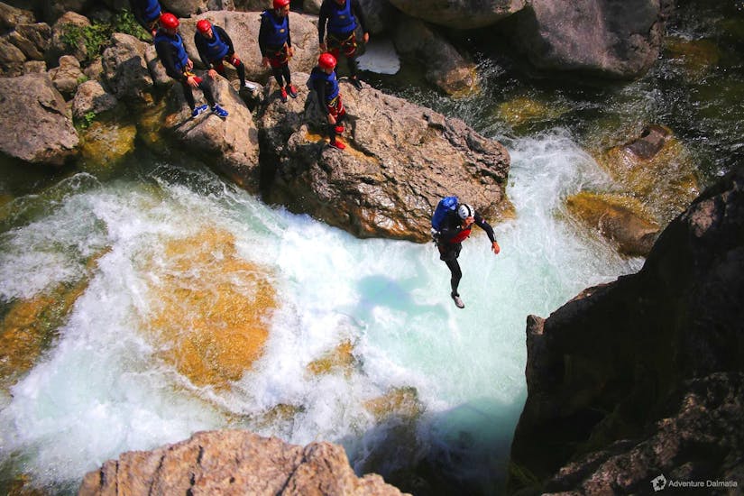 Una guida di canyoning di Adventure Dalmazia sta saltando in acqua durante il Canyoning per principianti con transfer dalla città di Split al fiume Cetina.