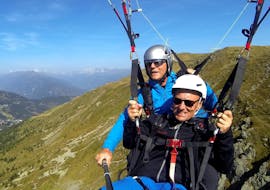 A man is smiling into the camera during his Tandem paragliding panorama flight from the Aineck with Flug Taxi fun and fly.
