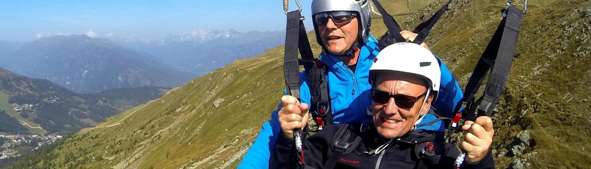 A man is smiling into the camera during his Tandem paragliding panorama flight from the Aineck with Flug Taxi fun and fly.