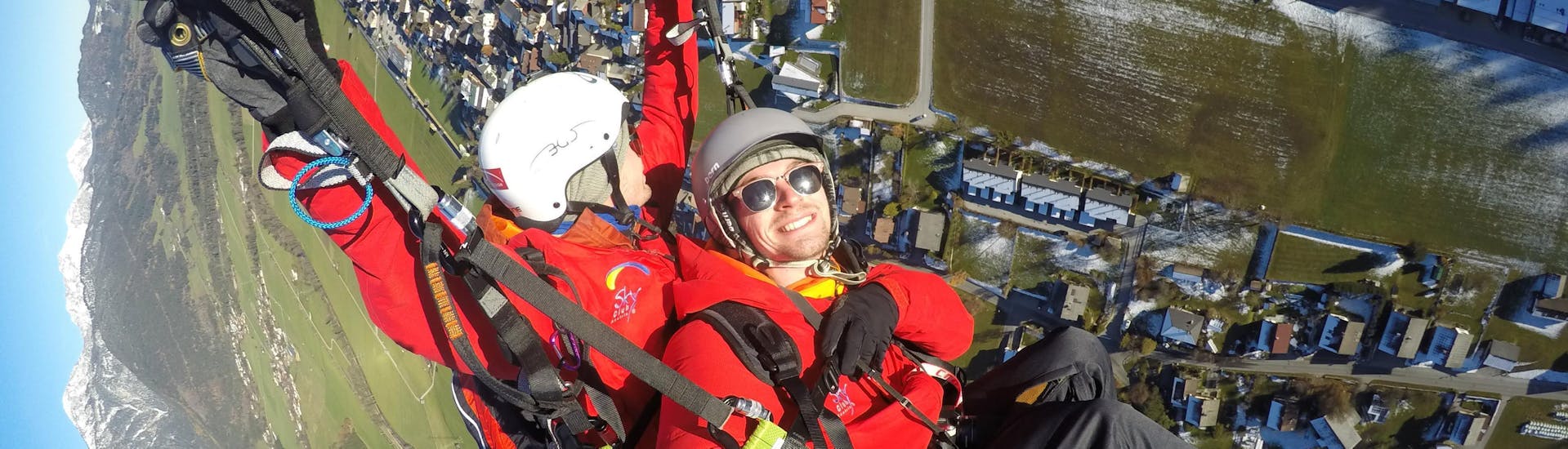 A customer smiles into the camera while the pilot safely steers the paraglider during the tandem paragliding from Stoderzinken with Flugschule Sky Club Austria Gröbming.