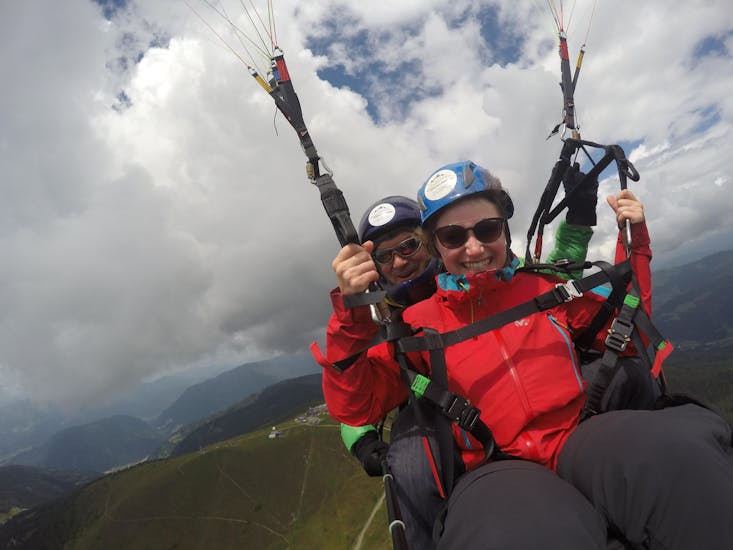Woman and pilot smiling happily into the camera while Tandem Paragliding over Lake Ossiach - Long Distance Flight with Flycenter Ossiachersee