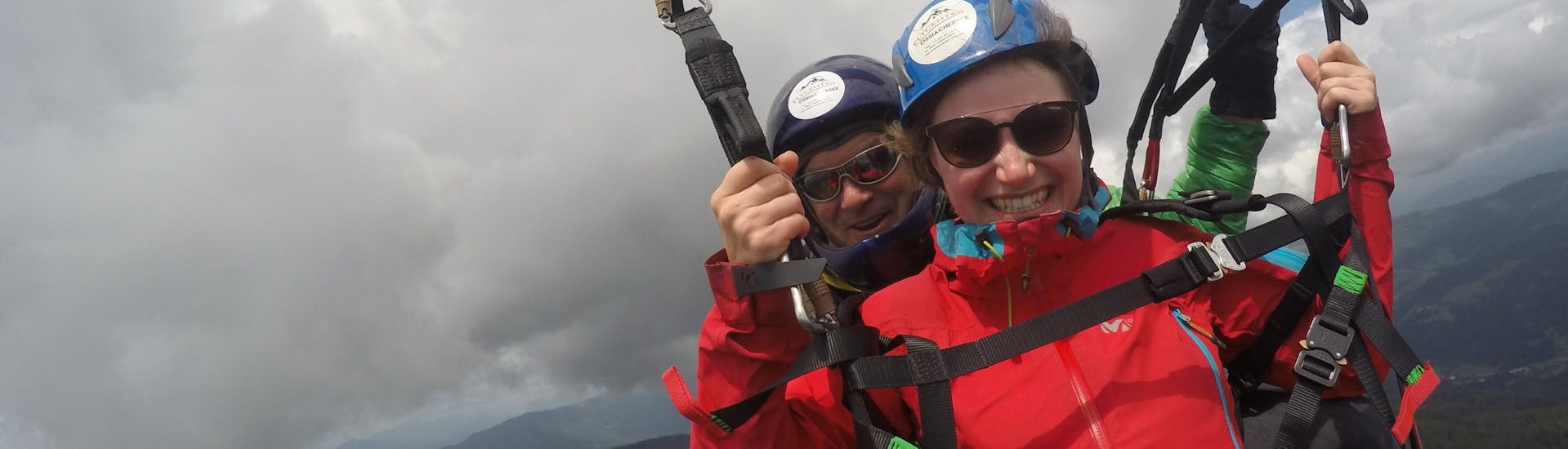 Vrouw en piloot lachen gelukkig in de camera tijdens het tandem paragliden boven de Ossiacher See - langeafstandsvlucht met Flycenter Ossiachersee