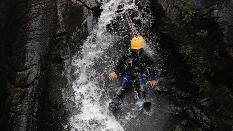 A person is standing on the ridge of a rock formation while water is falling down on him on his canyoning tour with ROCROI.