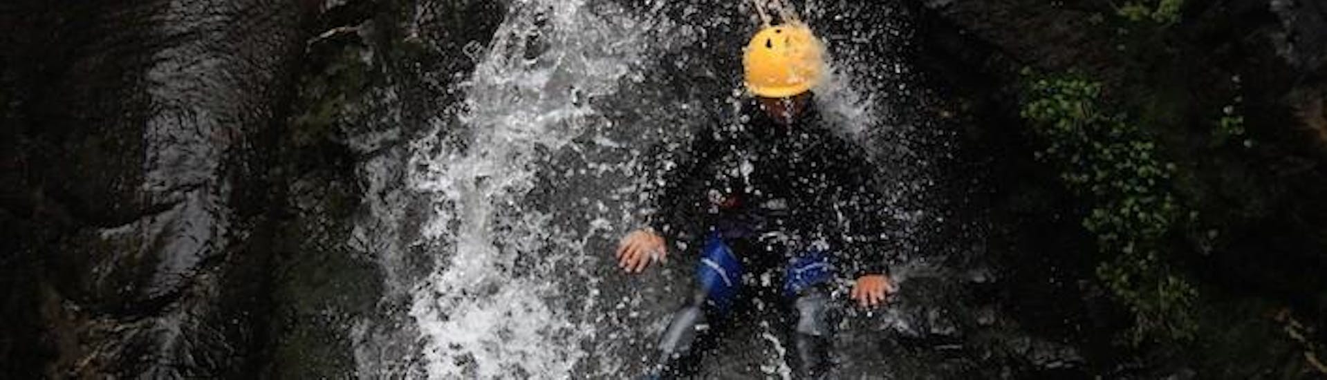 A person is standing on the ridge of a rock formation while water is falling down on him on his canyoning tour with ROCROI.