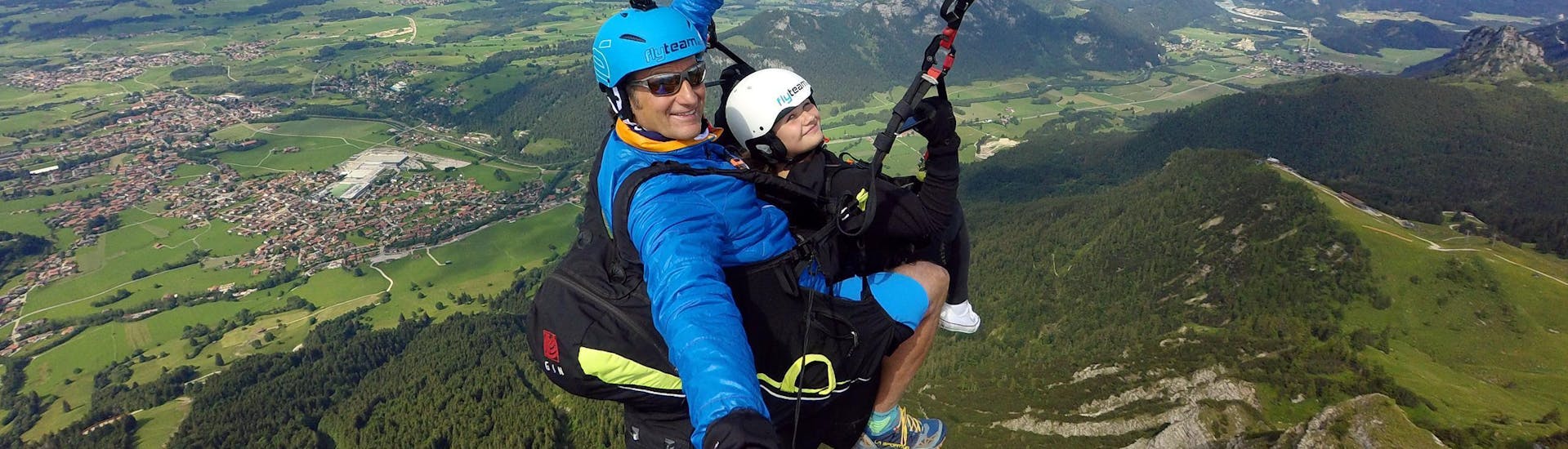 A tandem pilot from FlyTeam and his young passenger are soaring high above the Allgäu Prealps during the Tandem Paragliding "Panorama" from Breitenberg.
