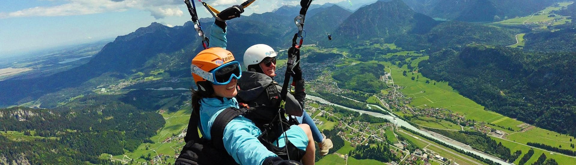 Eine Tandempilotin von FlyTeam und ihre Passagierin schweben beim Tandem-Gleitschirmfliegen "Panorama" vom Hahnenkamm hoch über Reutte in Tirol.