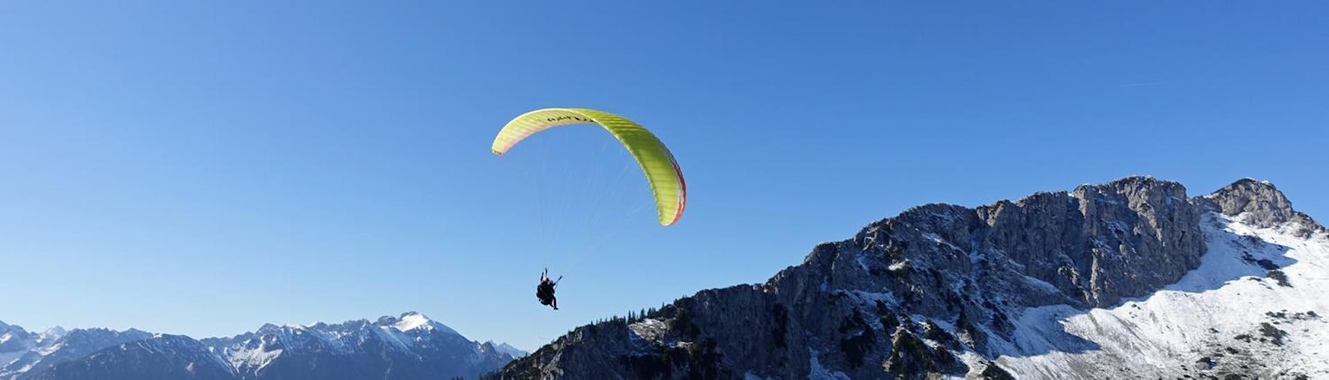 Beim Tandem Paragliding "Streckenflug" im Allgäu und in Tirol schwebt ein Gleitschirm von FlyTeam hoch über den Bergen.