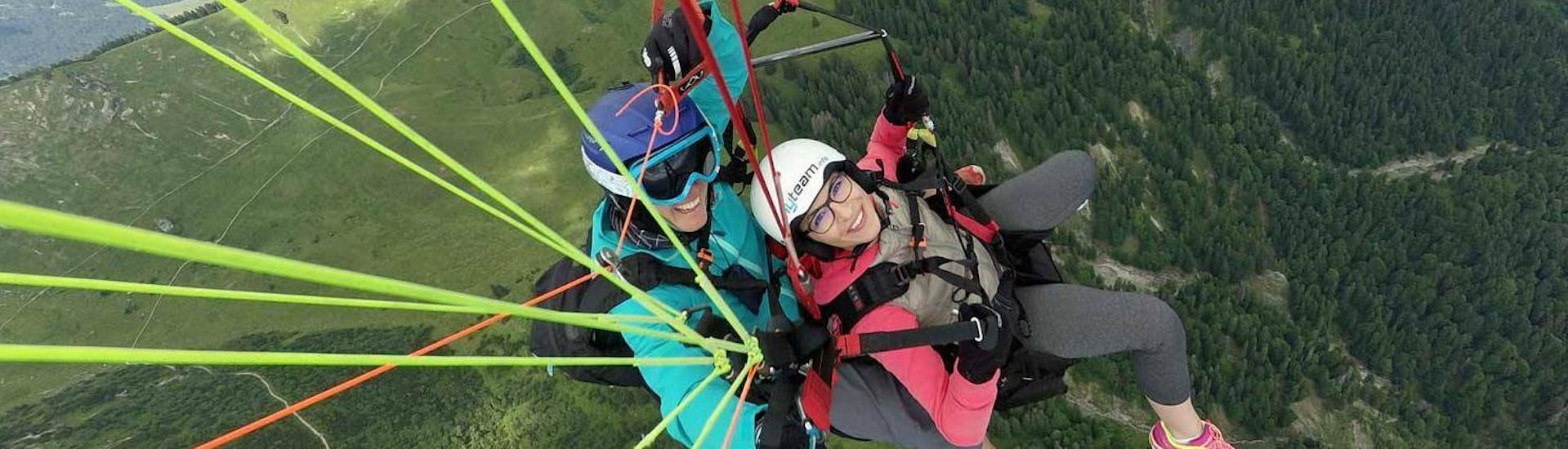 A tandem pilot from FlyTeam and his passenger are flying over the green mountain landscape during the Tandem Paragliding "Full Day" in Allgäu and Tyrol.