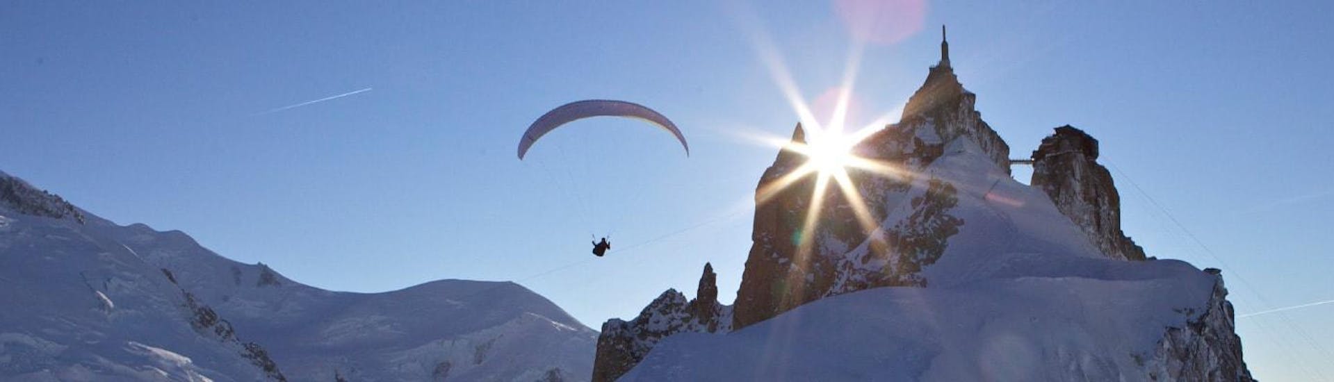 Ein Gleitschirmpilot von Kailash Paragliding führt einen Tandem-Flug mit dem Gleitschirm vom Plan de l'Aiguille vor einer Bergkulisse durch.