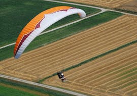 A paragliding pilot is flying over a field during their Tandem Paragliding "Discovery" - Chartreuse with Prévol Parapente.