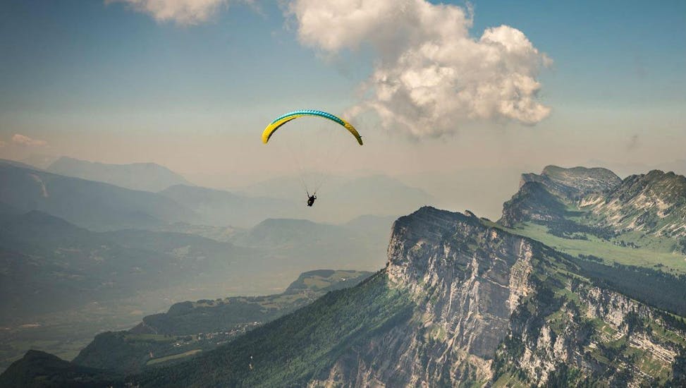 A paragliding pilot is flying over the Chartreuse massif during their Tandem Paragliding "Sensation" - Chartreuse with Prévol Paragliding.