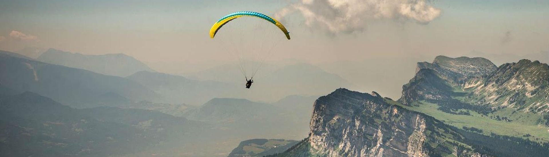 A paragliding pilot is flying over the Chartreuse massif during their Tandem Paragliding "Sensation" - Chartreuse with Prévol Paragliding.