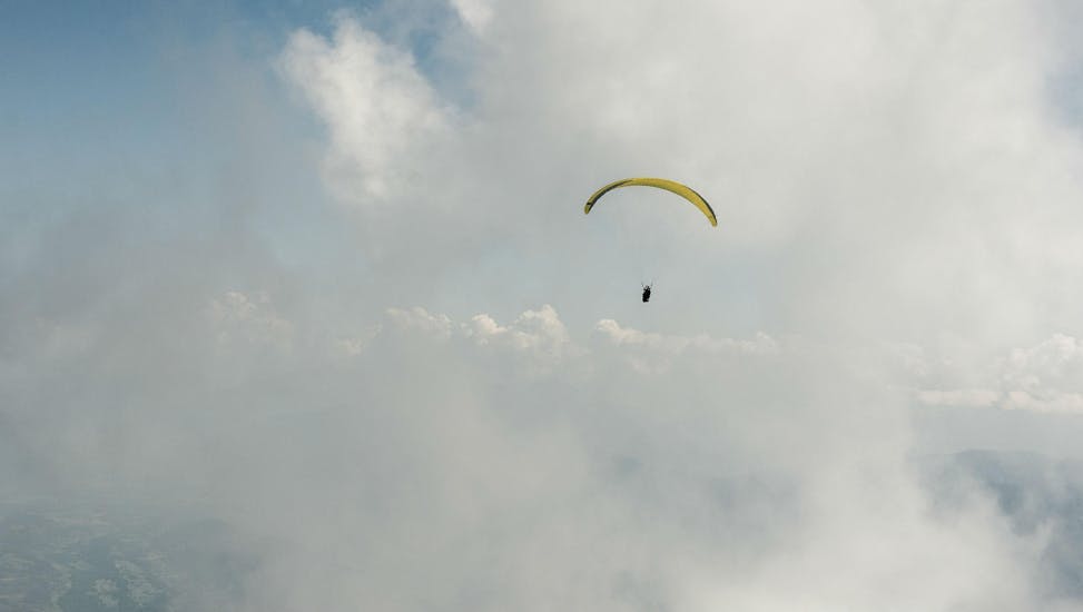 A paraglider is flying among the clouds during their Tandem Paragliding "Performance" - Chartreuse with Prévol Paragliding.