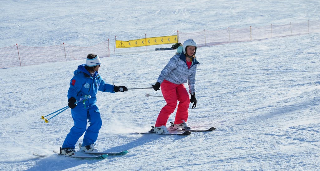 An instructor from the European Ski School in Les Deux Alpes accompanies a female skier in her first steps on skis during a private ski lesson for adults.