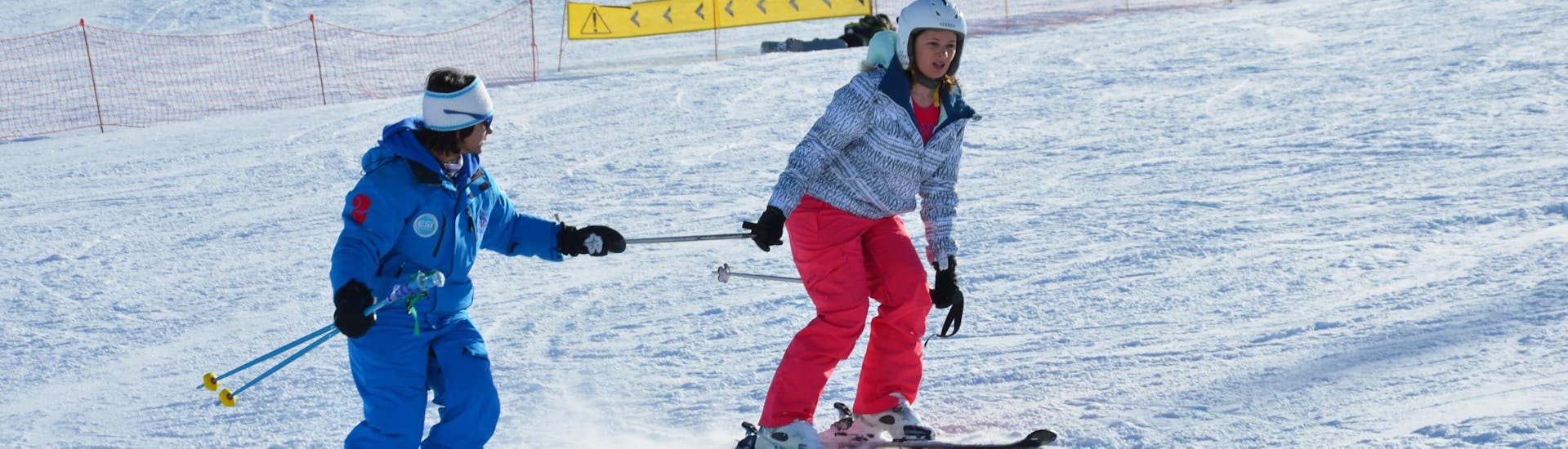 Een instructeur van de Europese Skischool in Les Deux Alpes begeleidt een vrouwelijke skiër in haar eerste stappen op ski's tijdens een privé skiles voor volwassenen.