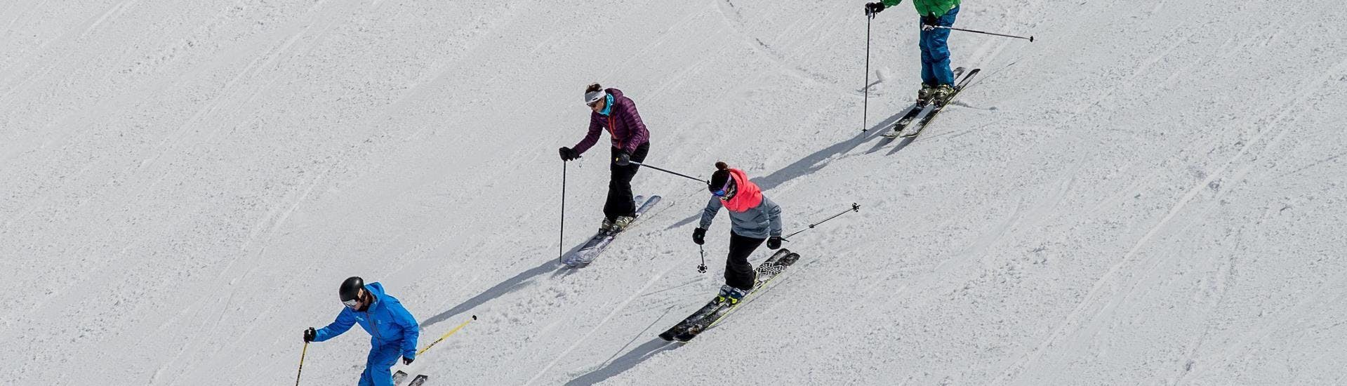 Three skieres are following their ski instructor from the ski school Ski Cool in skiing down a ski slope during one of their Private Ski Lessons for Adults - School Holiday - All Levels in the ski resort of Val Thorens.