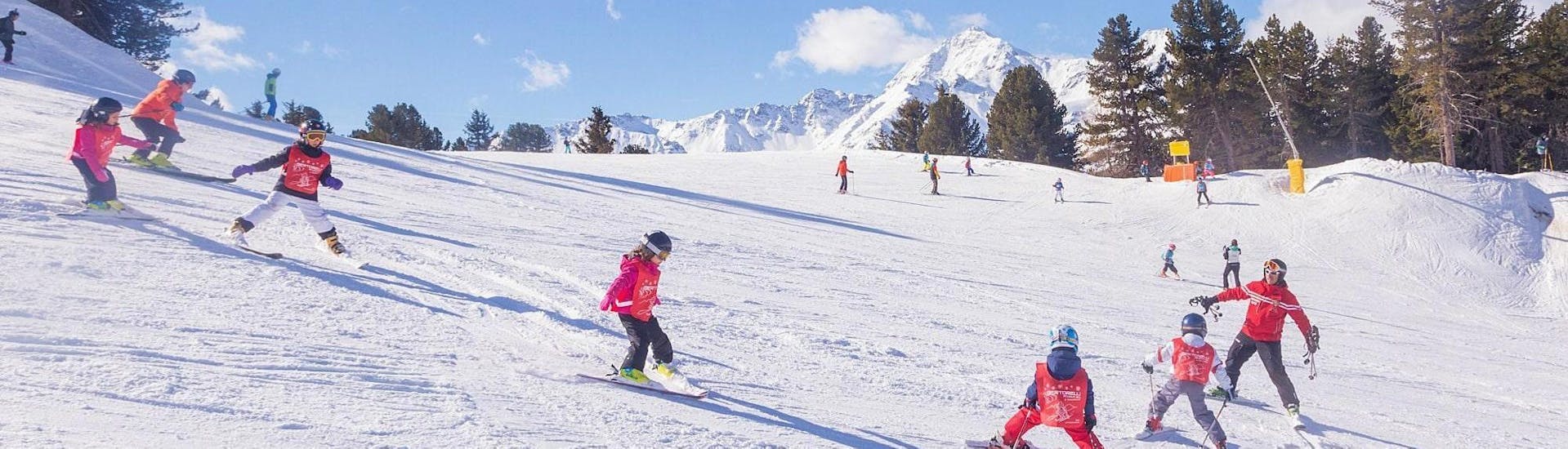 De skileraar van Sertorelli Skischool Bormio staat op de piste met de deelnemers tijdens de skilessen voor kinderen (4-12 jaar) voor gevorderden - hele dag