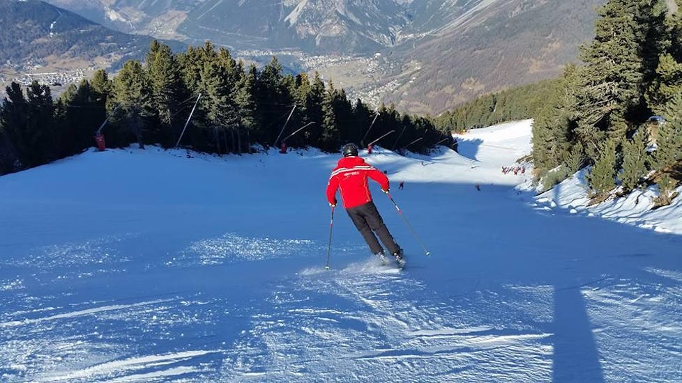 The ski instructor from Sertorelli Ski School Bormio is skiing on the slope in front of a participant of the Private Ski Lessons for Adults for all Adults.