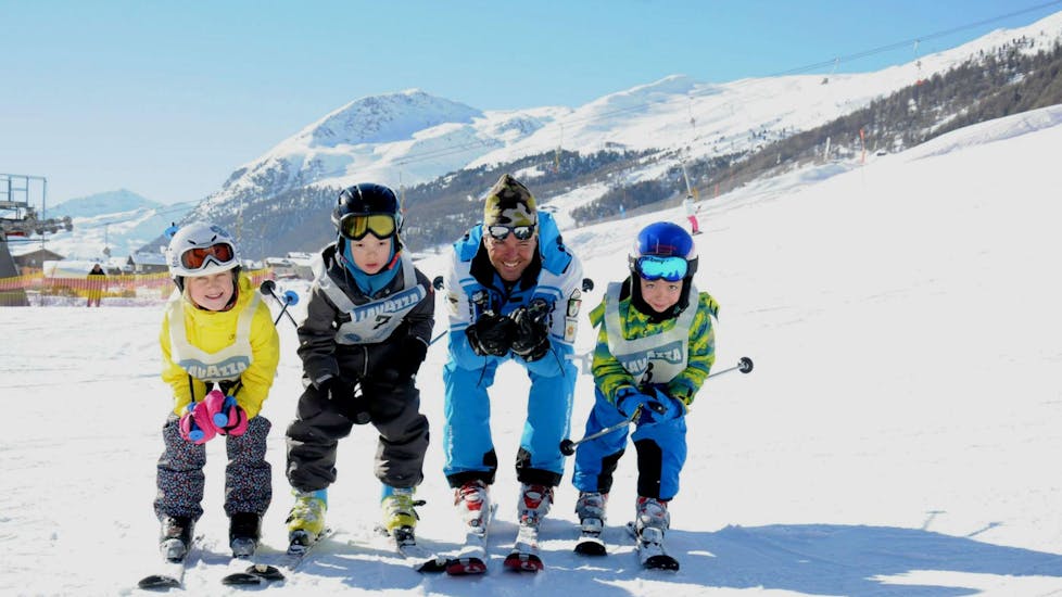 Drie kinderen genieten van hun Kinderskilessen Halve Dag (3-4 j.) - Beginners naast hun ski-instructeur van de skischool Scuola di Sci e Snowboard Livigno Italy. 