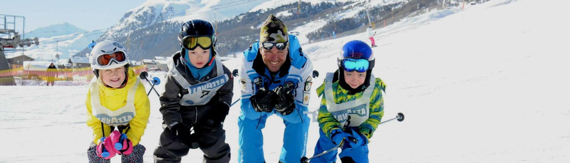 Trois enfants profitent de la demi-journée de cours de ski pour enfants (3-4 ans) - débutants avec leur moniteur de ski de l'école de ski Scuola di Sci e Snowboard Livigno Italie.