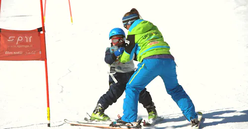 Private Ski Lessons for Kids & Teens of All Ages from Scuola di Sci e Snowboard Livigno Italy A teacher supports a child while circumventing the obstacles on the slope during the Private Ski Lessons for Kids (5-12 y.) - All Levels of the ski school Scuola di Sci e Snowboard Livigno Italy.