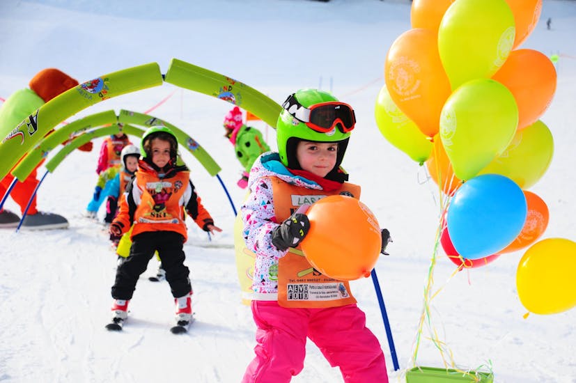 Le Lezioni di sci per bambini (4-13 anni) - Tutti livelli della Scuola di Sci AEvolution Folgarida si stanno svolgendo nel campo scuola; finiti gli ostacoli la bambina si merita un palloncino.