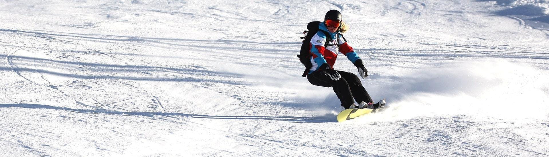 Une snowboardeuse descend une pente ensoleillée pendant un de ses cours de snowboard pour enfants et adultes - journée complète - niveau expérimenté dans la station de ski d'Ischgl.