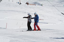 Un instructor de esquí está ayudando a un niño a hacer los primeros descensos en las clases de esquí para adultos - Principiantes, de la escuela de esquí Skischule Ischgl Schneesport Akademie.