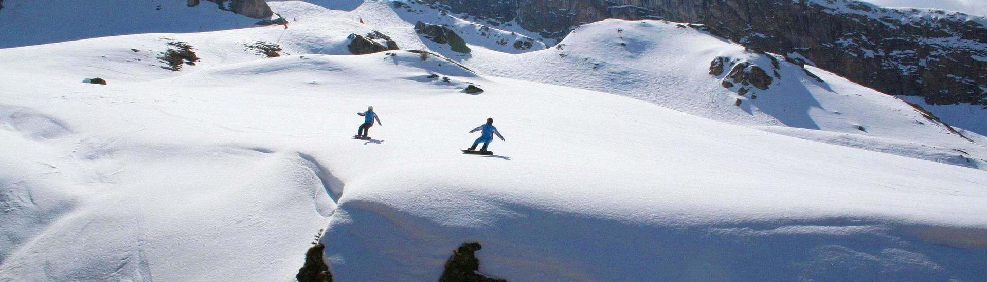 Ein Snowboardlehrer und sein Schützling gleiten im Rahmen des Angebots Privater Snowboardkurs für Kinder & Erwachsene - Alle Levels im Skigebiet Ischgl eine unberührte Pulverschneepiste hinunter.