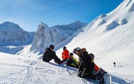 Gli snowboarder sono seduti sulla neve in mezzo alla montagna durante le lezioni di snowboard (a partire da 8 anni) per tutti i livelli con Evolution 2 Val d'Isère.
