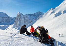Los snowboarders están sentados en la nieve en medio de la montaña durante sus clases de snowboard (a partir de 8 años) para todos los niveles, con Evolution 2 Val d'Isère.