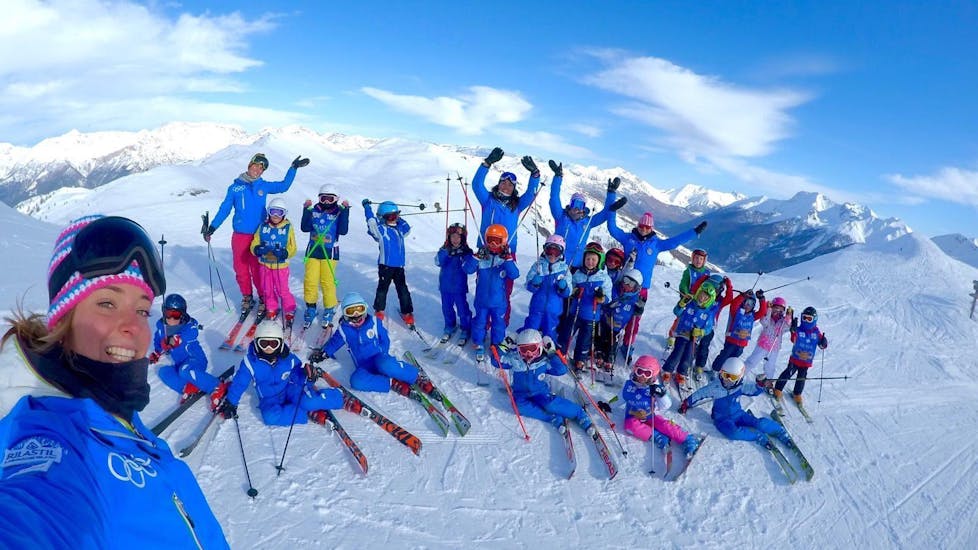 Een groep kinderen en hun ski-instructeurs van de skischool Scuola di Sci Olimpionica poseren voor een foto op de top van de berg in Sestriere. Dit voordat ze beginnen met hun Kinderskilessen (5-12 j.) - Gevorderden