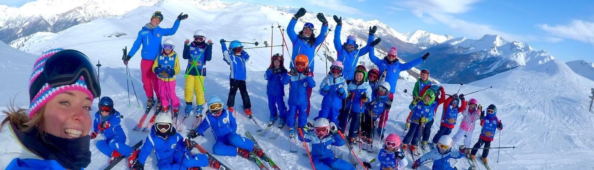 Een groep kinderen en hun ski-instructeurs van de skischool Scuola di Sci Olimpionica poseren voor een foto op de top van de berg in Sestriere. Dit voordat ze beginnen met hun Kinderskilessen (5-12 j.) - Gevorderden