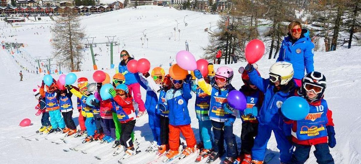 Een groep kinderen en hun ski-instructeur van de ski-school Scuola di Sci Olimpionica poseren voor een foto op de top van de berg in Sestriere. Dit voordat ze beginnen met hun Kinderskilessen (5-12 j.) - Beginner.