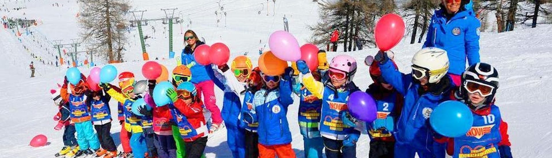 Un groupe d'enfants et leurs moniteurs de ski de l'école de ski Scuola di Sci Olimpionica posent pour une photo au sommet de la montagne à Sestrières, avant de commencer leur Premier Cours de ski Enfants (5-14 ans).