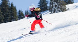 Eine junge Skifahrerin rast während ihrem privaten Skikurs für Kinder für alle Levels mit der Schneesportschule Balderschwang die Pisten hinunter während ihr Lehrer sie beobachtet. 