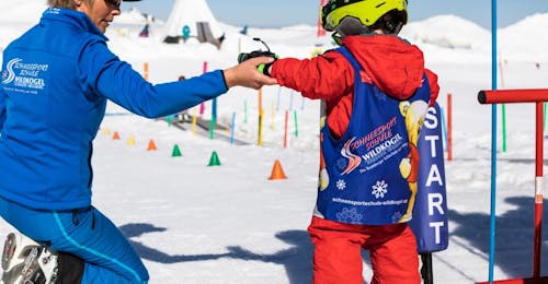 Kids Ski Lessons (3-14 y.) for All Levels - Half Day from Schneesportschule Wildkogel An instructor helps a small child as it takes it first steps on skis during Kids Ski Lessons (3-14 y.) for All Levels - Halfday with Schneesportschule Wildkogel.