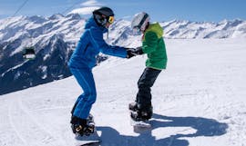 Ein Lehrer hilft einem Kind bei der richtigen Haltung auf dem Snowboard während des Snowboardkurses für Kinder und Erwachsene aller Levels in der Schneesportschule Wildkogel.