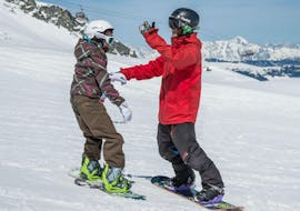 A snowboard instructor is helping a pupil during snowboarding lessons BOBOs kids club for beginner with Ski Dome Viehhofen.