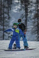 Maestro di snowboard che assiste un bambino durante una delle lezioni di snowboard per bambini e adulti di tutti i livelli a Sauze d'Oulx. 