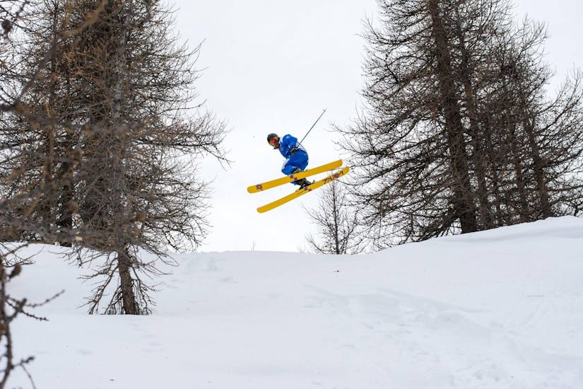 Il maestro di sci salta in aria in una foresta durante una delle lezioni private di sci freestyle per tutti i livelli a Sauze d'Oulx.