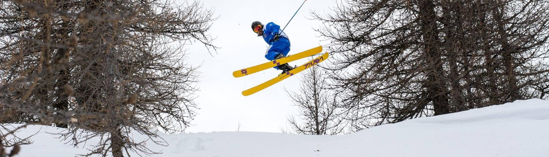 The ski instructor jumps into the air in a forest during one of the private freestyle ski lessons for all levels in Sauze d'Oulx.