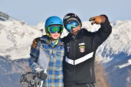 Un enfant heureux avec son moniteur pendant le cours particulier de snowboard avec Cimaschool Plan de Corones.