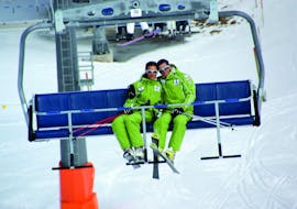 Twee skileraren van skischool Club Alpin in Grän zitten op een stoeltjeslift om het ontmoetingspunt voor skilessen voor volwassenen te bereiken.