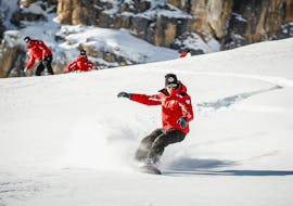 Le moniteur de snowboard de l'école de ski Scuola Sci Cortina dirige la descente sur la piste pendant les cours particuliers de snowboard pour enfants et adultes - tous niveaux.