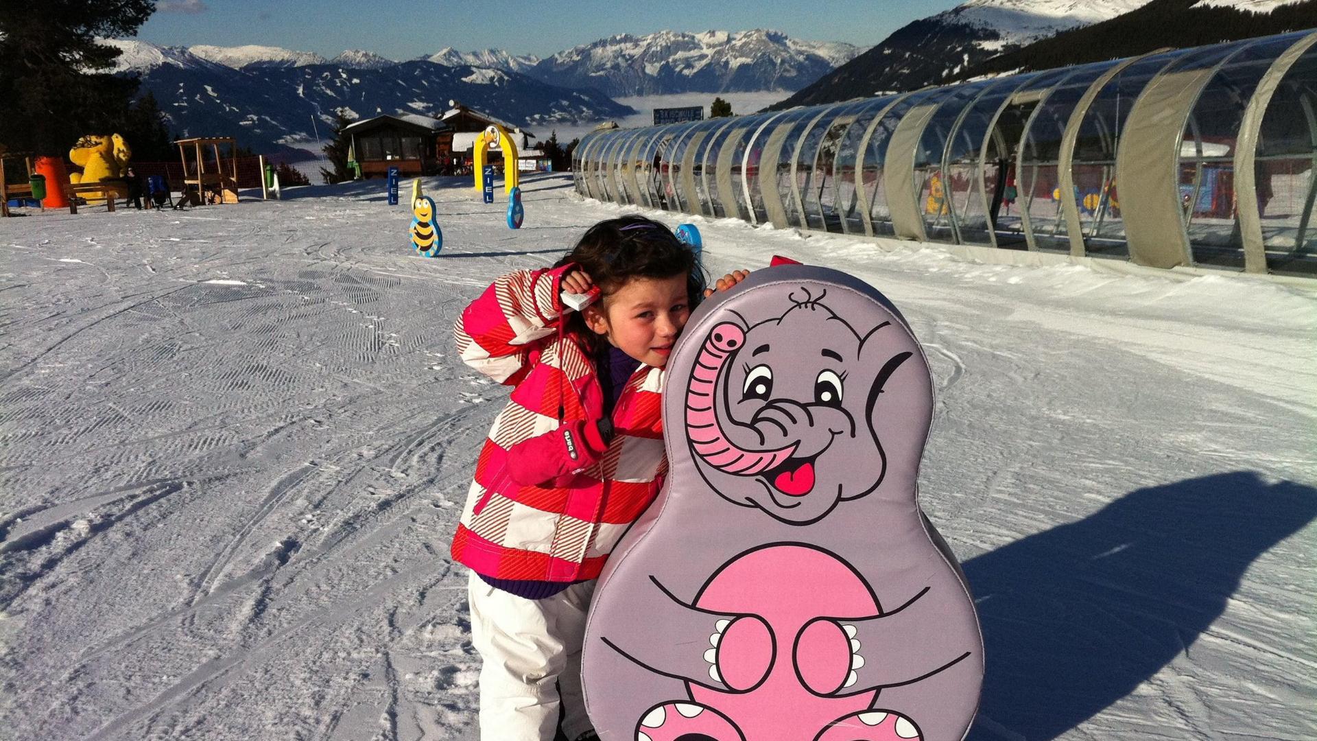 A little girl is posing for a photo with a cute elephant during the Kids Ski Lessons (from 6 years) - Advanced organised by the ski school Skischule Arena in Zell am Ziller.