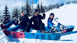 Eine glückliche Gruppe von Snowboardern, die während des privaten Snowboardkurses für Kinder und Erwachsene aller Niveaus im Schnee sitzen. 